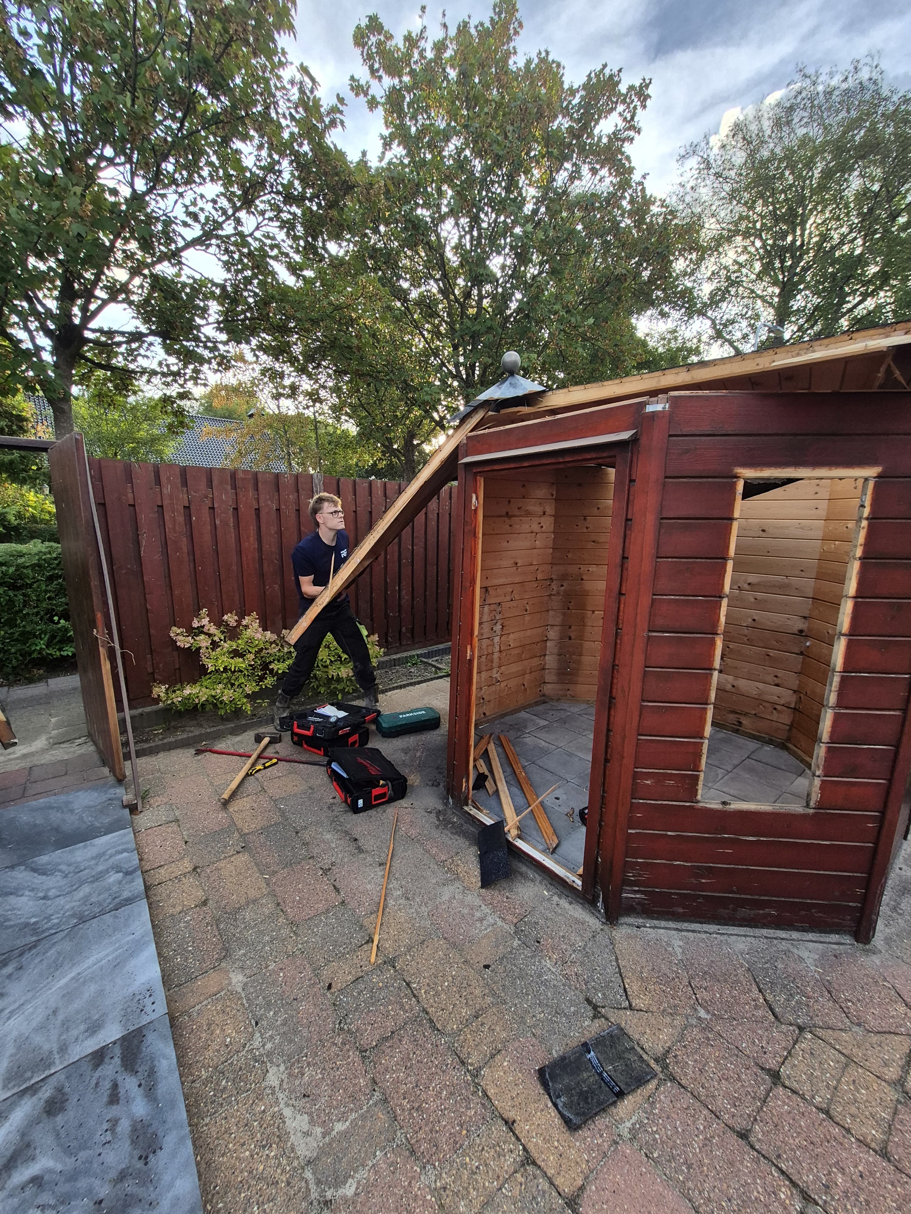 Het dak van een houten tuinhuisje wordt gesloopt in Ouddorp.