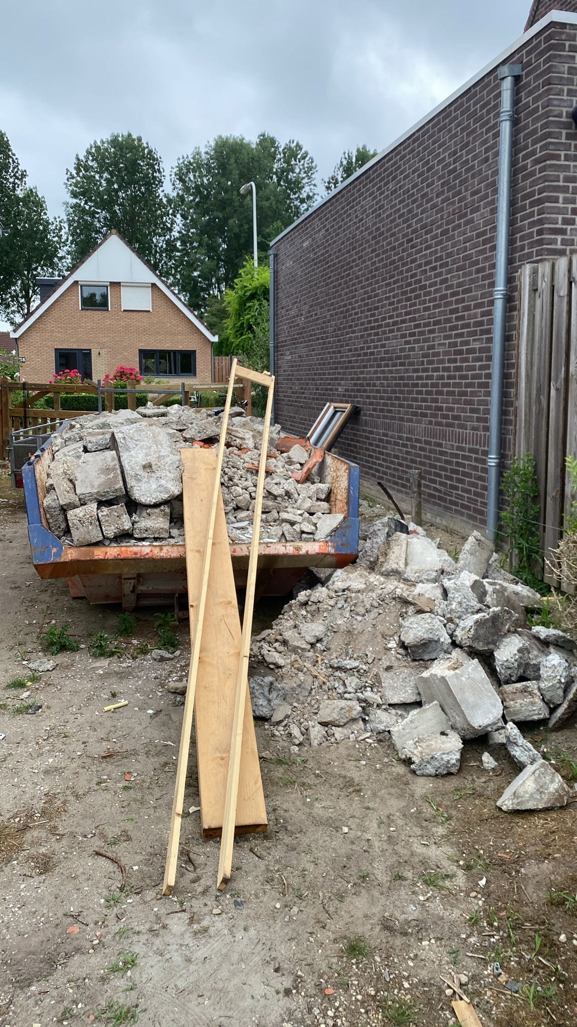 Container vol gesloopt betonpuin naast de schuur, brokken van de oude fundering opgestapeld.